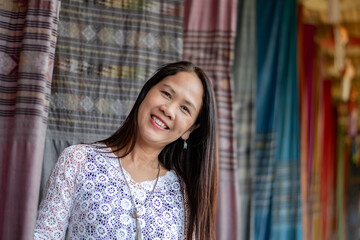 Asian mid adult woman holds woven fabric which was decorated on ceiling of local cafe for tourist watching and taking photos, soft focus, happiness of humans concept.