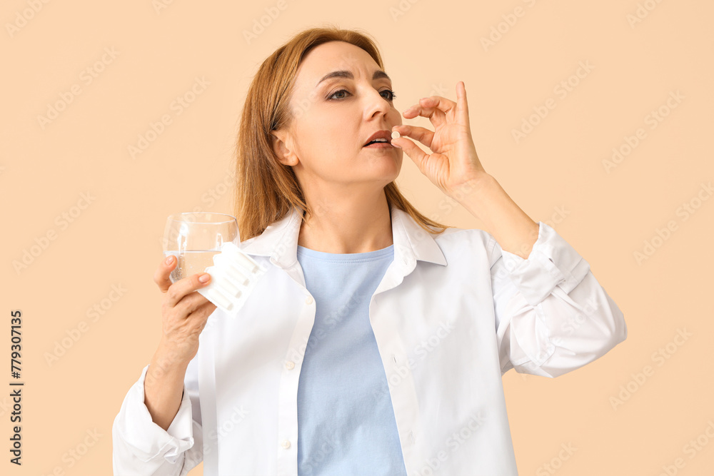 Mature woman taking pill on beige background. Menopause concept