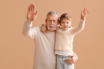 Wall Mural - Grandfather with his happy cute little grandson waving hands on beige background