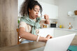 Hurrying young African-American woman eating breakfast and looking at wristwatch in kitchen