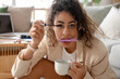 Hurrying African-American businesswoman with coffee cup applying mascara at home, closeup