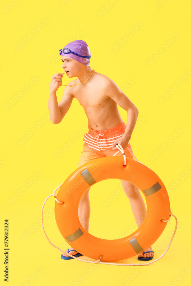 Cute little boy with ring buoy and whistle on yellow background
