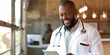 © Muhammad - A happy and smiling African American male doctor wearing a white coat is working on a tablet computer at his office. Medical Health Care Professionals Working with Test Results,