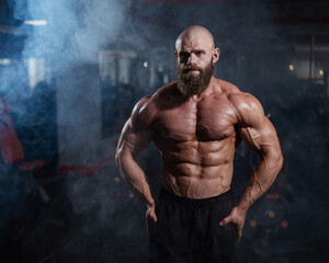 Wall Mural - Muscular bald man posing shirtless. Bodybuilder showing off his shape in the gym. 