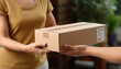 © cabado - Courier hand delivering a cardboard box during day to a woman at her home on blurred urban background. Messenger and delivery concept.