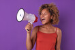 Young bold ethnic African American woman student shouting in megaphone reporting presence racial discrimination or gender inequality dressed in casual clothes stands in purple studio. Protest, strike