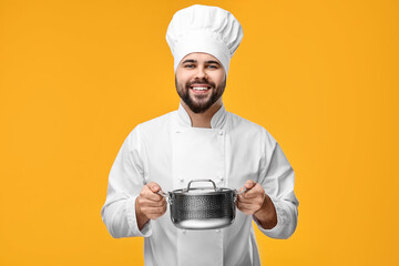 Sticker - Happy young chef in uniform holding cooking pot on orange background