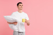 Happy man in pyjama holding pillow and cup of drink on pink background, space for text