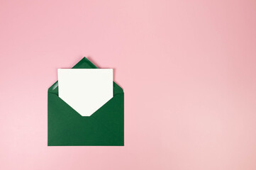 Top view of dark green envelope, white card on pink background. Post flat lay. Copy space.