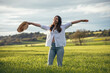 © Westend61 - Carefree woman holding hat and standing under cloudy sky at field