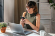 © Westend61 - Smiling businesswoman using smart phone near laptop in office