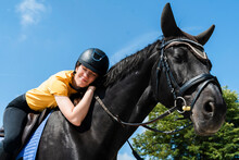Smiling Instructor With Eyes Closed Riding Black Horse On Sunny Day