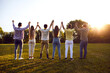© Studio Romantic - Back view of a group of happy friends standing in a row holding hands with their hands up outdoors. Young men and women spending time together with raised arms enjoying sunset sky.
