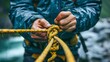 © pisan - Close up of Adventurer Tying Knot in Yellow Rope During Rainy Weather Outdoors, Concept of Safety and Preparedness in Extreme Conditions