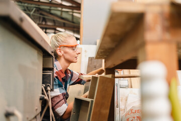 Wall Mural - In a bustling carpenter's shop, a young woman craftsman expertly navigates her workshop, merging traditional woodwork skills with modern equipment to create hand-made furniture