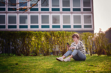 Sticker - Seated on the grass, a young woman lost in her smartphone embodies the harmony of technology and nature in an urban park at dusk.