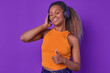 Young cheerful emotional African American woman in wireless headphones shows thumbs up and closes eyes with pleasure hearing music track of favorite singer stands in purple studio. Podcast, audio book