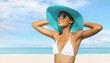 © amedeoemaja - Happy young woman at the beach side, wearing a turquoise sun hat, blue sunglasses and bikini, portrait of African latin American woman in sunny summer day with blue sky, concept of a summer holiday