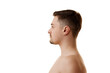 © Lustre Art Group  - Side view portrait of shirtless young man with brunette hair and stubble posing half-naked against white studio background. Concept of natural beauty, male health, anti-aging, spa procedures.
