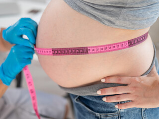 Wall Mural - Doctor measuring the volume of a pregnant woman's abdomen using a centimeter tape. 