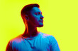 Serious young athletic man posing in casual attire in neon light against vibrant yellow studio background. Concept of natural beauty, male health, anti-aging, spa procedures, cosmetic products.