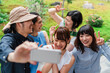 © Studio Marmellata - A group of five cheerful Japanese friends taking a selfie together outdoors, with a man holding the phone and everyone smiling broadly