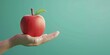 A hand holding a red apple with a green leaf on top. Concept of freshness and health, as apples are often associated with these qualities