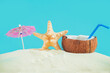 Coconut with a straw, shells, starfish and a sun umbrella on the sand.