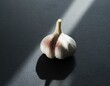 A solo garlic clove with the papery skin partially peeled, placed in the center of a dark, textured surface to highlight its organic form and texture.
