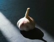 A solo garlic clove with the papery skin partially peeled, placed in the center of a dark, textured surface to highlight its organic form and texture.