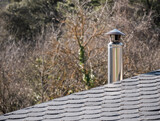Fototapeta Londyn - Metal chimney placed on a slate tile roof typical of the town houses of Bierzo and an autumn background of deciduous trees without leaves