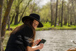 © Sid Smith - Girl in a black hat flirtatiously looks at the camera holding a phone in her hands on the lake shore