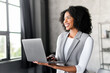 An upbeat African-American businesswoman engages with her computer, her smile suggesting a positive interaction or successful business venture. The blend of technology and business acumen