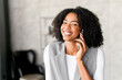 With a bright smile, this African-American businesswoman engages in a cheerful conversation over her phone, standing in a modern office setting that reflects connectivity and accessibility.
