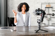 Charming businesswoman smiles warmly at the camera, her hand gesture suggesting a friendly greeting during a video presentation in a corporate setting, business coach recording video vlog, training