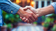 Two individuals engaging in a firm handshake, symbolizing agreement or greeting, with blurred background suggesting a casual outdoor setting.