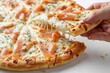 Close-up shot of a hand taking a slice of delicious smoked salmon pizza