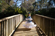 A pretty girl dancing flamenco in a typical gypsy dress with frills and fringes walks on a wooden bridge in a famous park in Seville, Spain. Her hair is tied back with a flower.