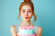 Happy young woman smiling and holding birthday cake with candle on light blue background. Minimal party concept.