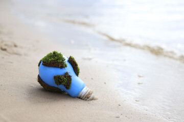 social problems. Earth Day. blue light bulb with green moss in the sand on the seashore