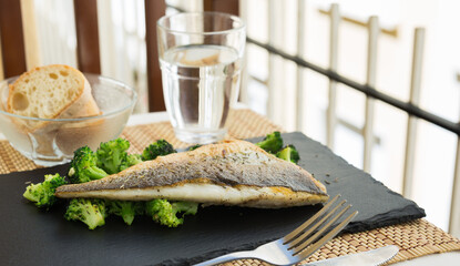 Wall Mural - Fried fillet of sea bass with garnish of broccoli on black warm stone plate