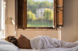 Naked young woman sleeping on the retro bed covering of white sheet in the rustic room of countryside building in the summer. Back view