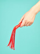 Red whip for adult role play games in woman's hand over turquoise blue background