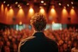 Rear view of a confident speaker at a podium facing a large, attentive audience in a conference hall.