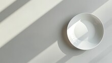 A White Round Plate On A Surface With Diagonal Shadow Patterns