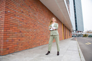 Wall Mural - Portrait of a successful business woman in front of modern business building. Young manager poses outside. Female business leader.
