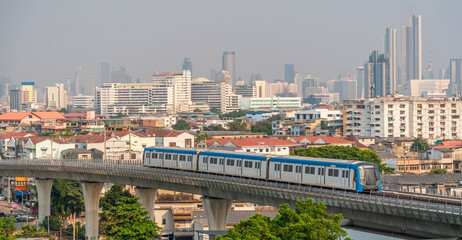 Wall Mural - City metro train carriage departs over an overpass bridge to the central part of the metropolis, tall skyscrapers are visible in the distance