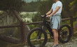 © Taras Grebinets - Close-up of a male cyclist riding an electric bike, a battery powered bicycle in the nature. Bike sharing city service. Male commuter renting an electric bike as eco public transport. Copy ad space