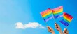 The image captures a moment of pride with two rainbow flags held up against a bright blue sky, symbolizing freedom and equality.