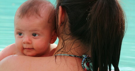 Wall Mural - Mother holding baby at the swimming pool, kissing baby showing love and affection